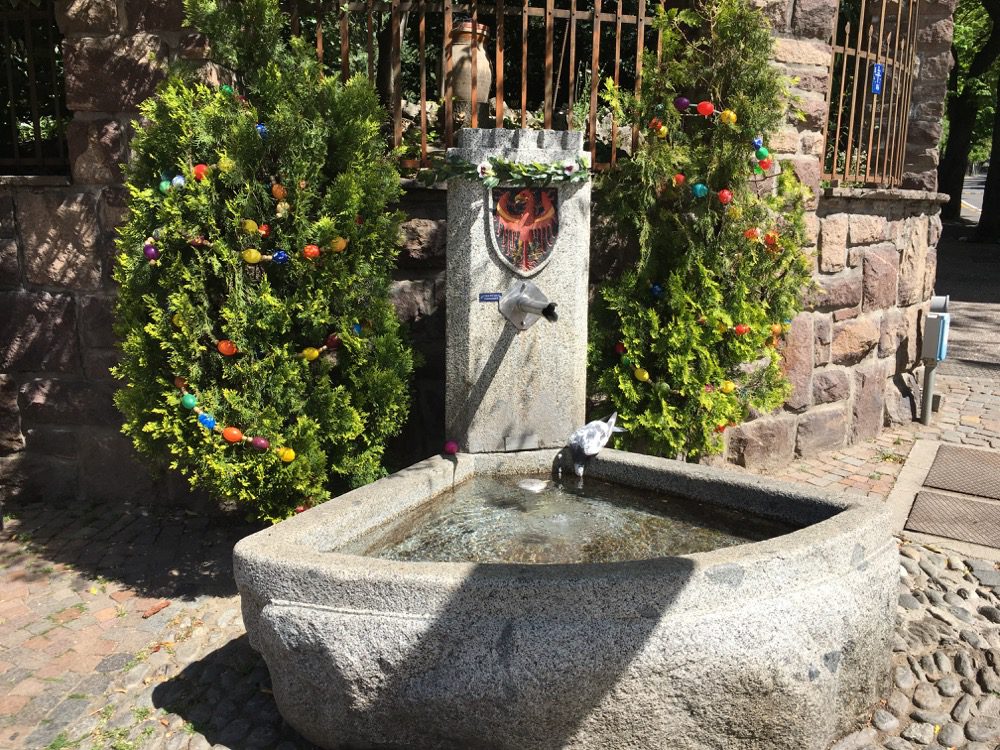 Man merkt, dass Ostern ist: Mit Ostereiern dekorierte Thujen an einem Brunnen in Meran (Meran, Meraner Land, Südtirol, April 2022).