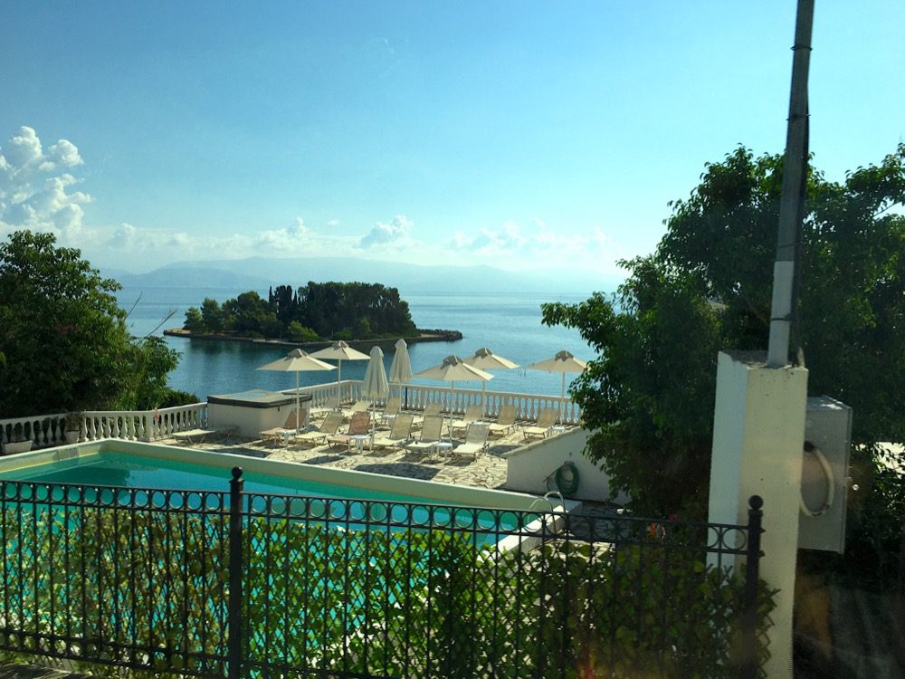 Ein schnelles Foto aus dem Bus nach Moraitika: Der Pool eines Hotels und die Insel 'Pondikonisi' vor der Ostküste von Korfu (Korfu, Ionische Inseln, Griechenland, 14.08.2022).