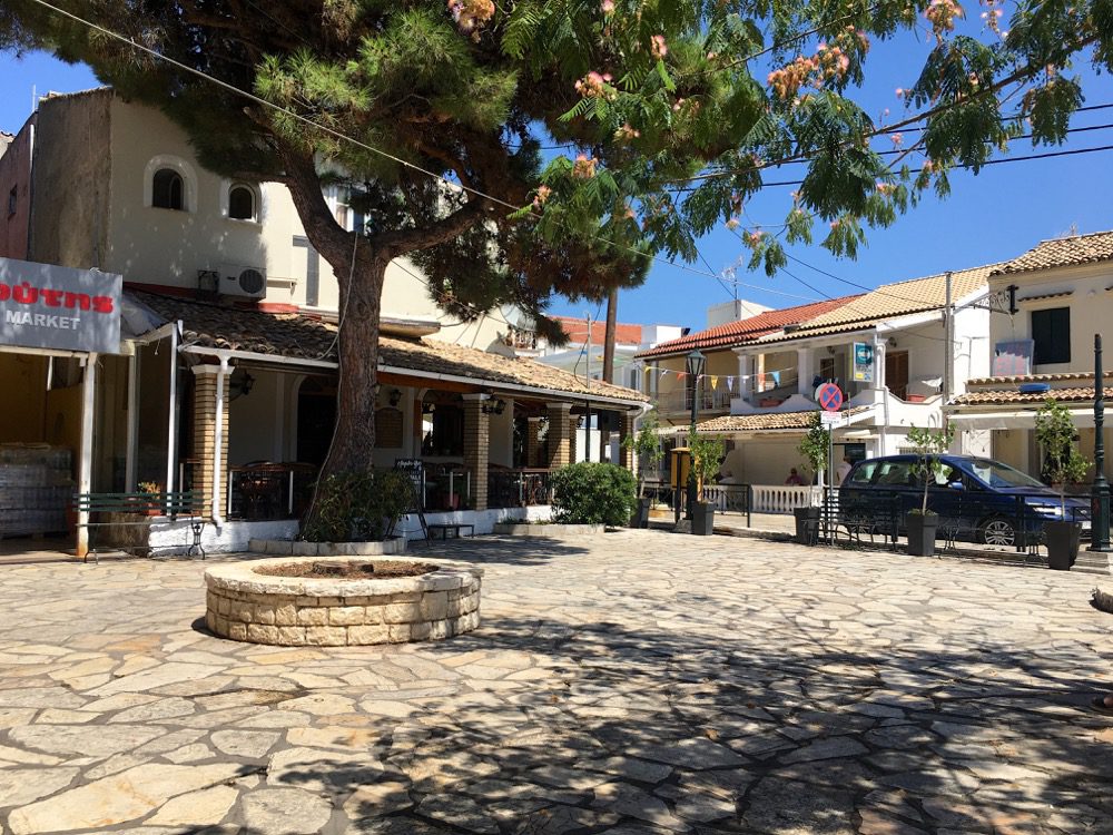 Nicht der Marktplatz, aber der Platz vor der Bushaltestelle in Kassiopi an der Westküste von Korfu (Korfu, Ionische Inseln, Griechenland, 17.08.2022). 