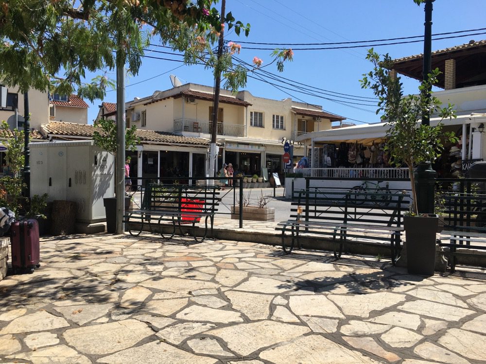 Nicht der Marktplatz, aber der Platz vor der Bushaltestelle in Kassiopi an der Westküste von Korfu (Korfu, Ionische Inseln, Griechenland, 17.08.2022). 